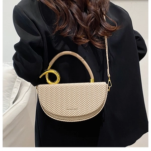 Detail of beige saddle bag with V-weave texture and golden knot handle on a black suit
