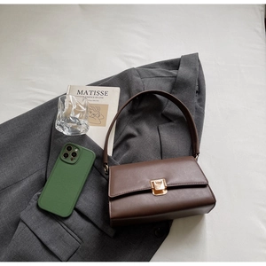 Close-up of a dark brown baguette bag with a gold square twist lock on a grey suit jacket