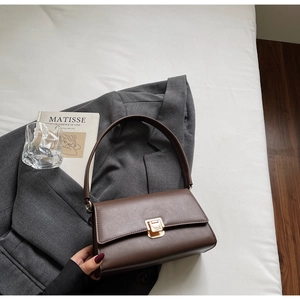 Detail of dark brown leather baguette bag with golden metal buckle on grey blazer