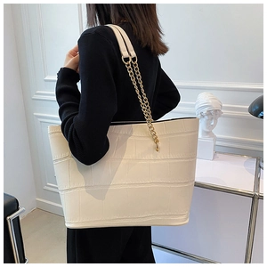 Detail of white crocodile texture tote bag featuring golden metal chain shoulder strap