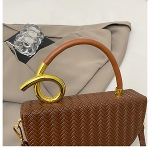 Detailed close-up of a woven brown handbag featuring a luxury gold metal knot handle