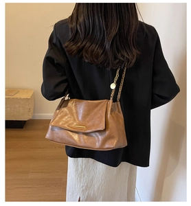 Detail of a brown leather tote bag with a gold metal chain strap worn by a model