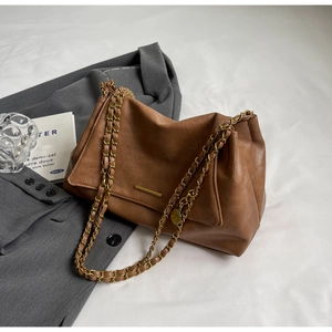 Detail of caramel leather bag with gold metal bar and woven chain on a grey blazer