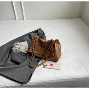 Flat lay of brown leather chain shoulder bag on white bed with lifestyle accessories