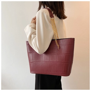 Detail of burgundy tote bag with crocodile texture and gold chain shoulder strap