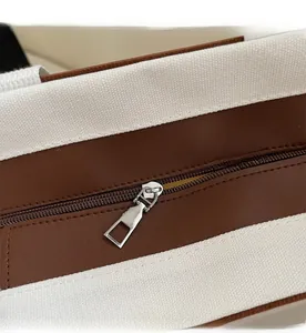 Detailed close-up of smooth silver metal zipper on canvas and brown leather tote bag