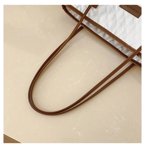 Detail of white quilted tote bag featuring brown leather straps and fashion label tag