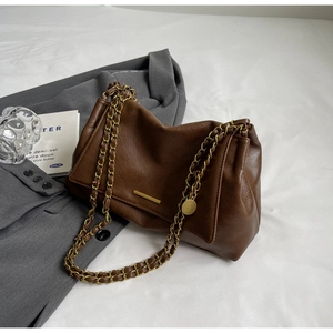 Detail of brown leather shoulder bag featuring gold chain strap and metal bar decoration