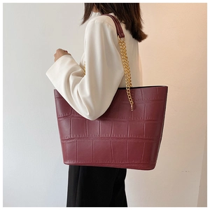 Detail of burgundy tote bag with crocodile embossing and gold chain strap on shoulder
