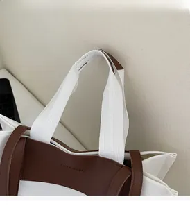 Close-up of white canvas tote with brown leather trim and reinforced handle stitching