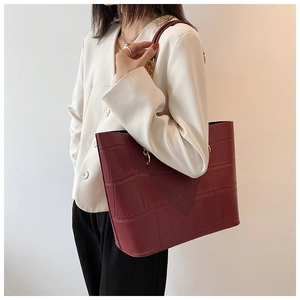 Detail of burgundy crocodile-embossed tote bag with golden hardware on a model