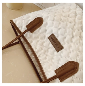Detail of white quilted tote bag with brown leather trim and fashion label on the front