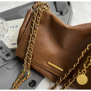Close-up of brown faux leather bag with gold hardware, chain strap and pendant charm