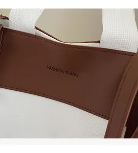 Detail of off-white canvas tote with brown leather stitching and embossed fashion logo