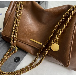 Close-up of textured dark brown leather bag with golden chain strap and metal buckle