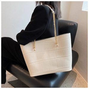 Close-up of creamy white crocodile-embossed leather tote bag with gold chain strap detail