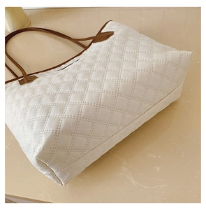 Detail of white quilted tote bag with brown leather straps on marble surface
