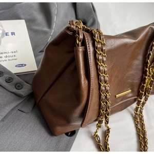 Close-up of brown textured leather bag with gold chain and minimalist metal bar detail