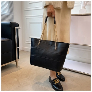 Detail of glossy crocodile pattern texture and gold chain strap on black tote bag