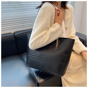 Detail of black crocodile texture tote bag with elegant gold metal chain straps