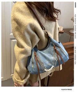 Detail of blue denim hobo bag with gold chain and pearl charm shown on shoulder