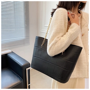 Detail of black crocodile pattern tote bag with gold chain strap on shoulder