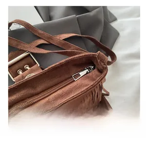 Close-up of smooth metal zipper and brown suede fringe detail on retro crossbody bag