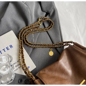 Detail of brown PU leather crossbody bag with metal chain strap and round pendant on fabric