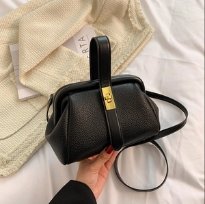 Elegant black lychee leather doctor bag with gold lock and top handle shown on white fabric