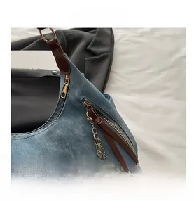 Detail of blue denim crescent bag with leather puller, gold zipper, and chain accent