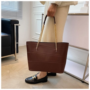 Detail of dark brown crocodile embossed tote bag with elegant golden chain handles