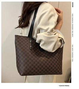 Side view of large brown monogram tote bag with long straps worn on a shoulder