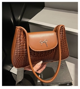 Detail of brown crocodile embossed leather handbag with silver bow metal clasp detail