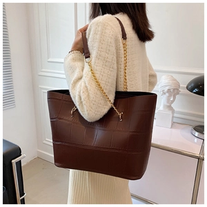 Detail of brown crocodile pattern tote bag with gold chain strap on female model