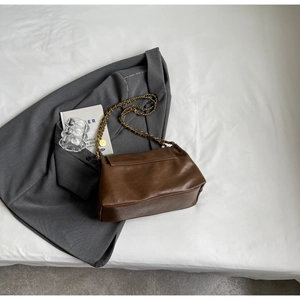 Detail of vintage brown leather tote bag with gold chain strap on grey blazer fabric