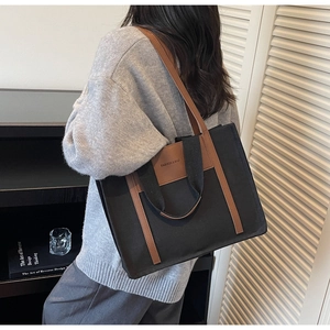 Detail of black canvas tote bag with brown leather straps shown on model for daily use
