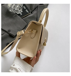Detail of beige shoulder bag showing gold twist lock and woven leather texture flap