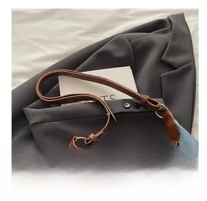 Detail of blue denim tote bag with brown leather strap and golden ring connector