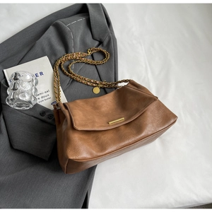 Close-up of brown textured leather shoulder bag with gold chain strap and metal clasp