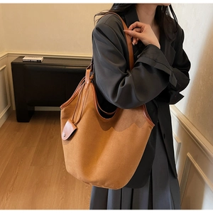 Détail du sac seau en daim beige avec bordure en cuir et bandoulière sur un modèle