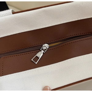Detail of silver metal zipper and brown leather trim on canvas tote bag with neat stitching