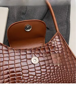 Detail of a brown crocodile pattern shoulder bag featuring a magnetic metal buckle closure