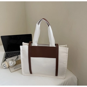 Large canvas tote bag with brown leather handles displayed next to a laptop and headphones