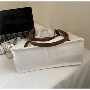 Detail of canvas tote bag with brown leather handles next to books and electronics