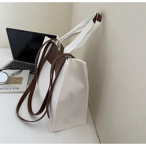 Detailed side view of a large canvas tote bag with leather straps on a workspace desk