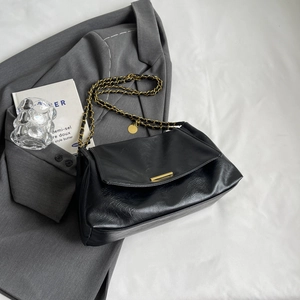 Elegant black glossy shoulder bag with gold chain strap and chic metal bar on grey blazer