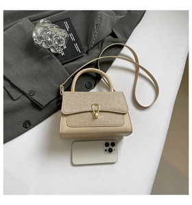 Detail of beige leather crossbody bag with shimmering gold flap and metal horsebit clasp