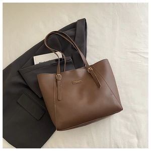Détail d'un sac cabas en cuir marron avec texte embossé et boucle dorée sur blazer