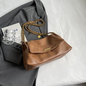 Brown vintage leather shoulder bag with gold hardware and chain strap on a grey blazer