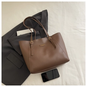 Détail du cabas en cuir marron café avec boucle dorée sur un blazer gris chic